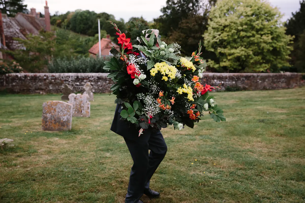 Man carrying a huge bunch of flowers across a churchyard, his face hidden behind it