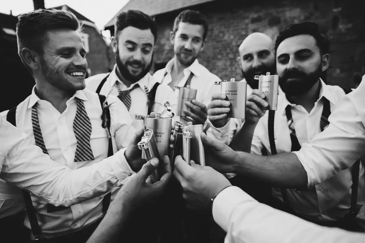 Groomsmen saying cheers with their hip flasks at Oxford wedding