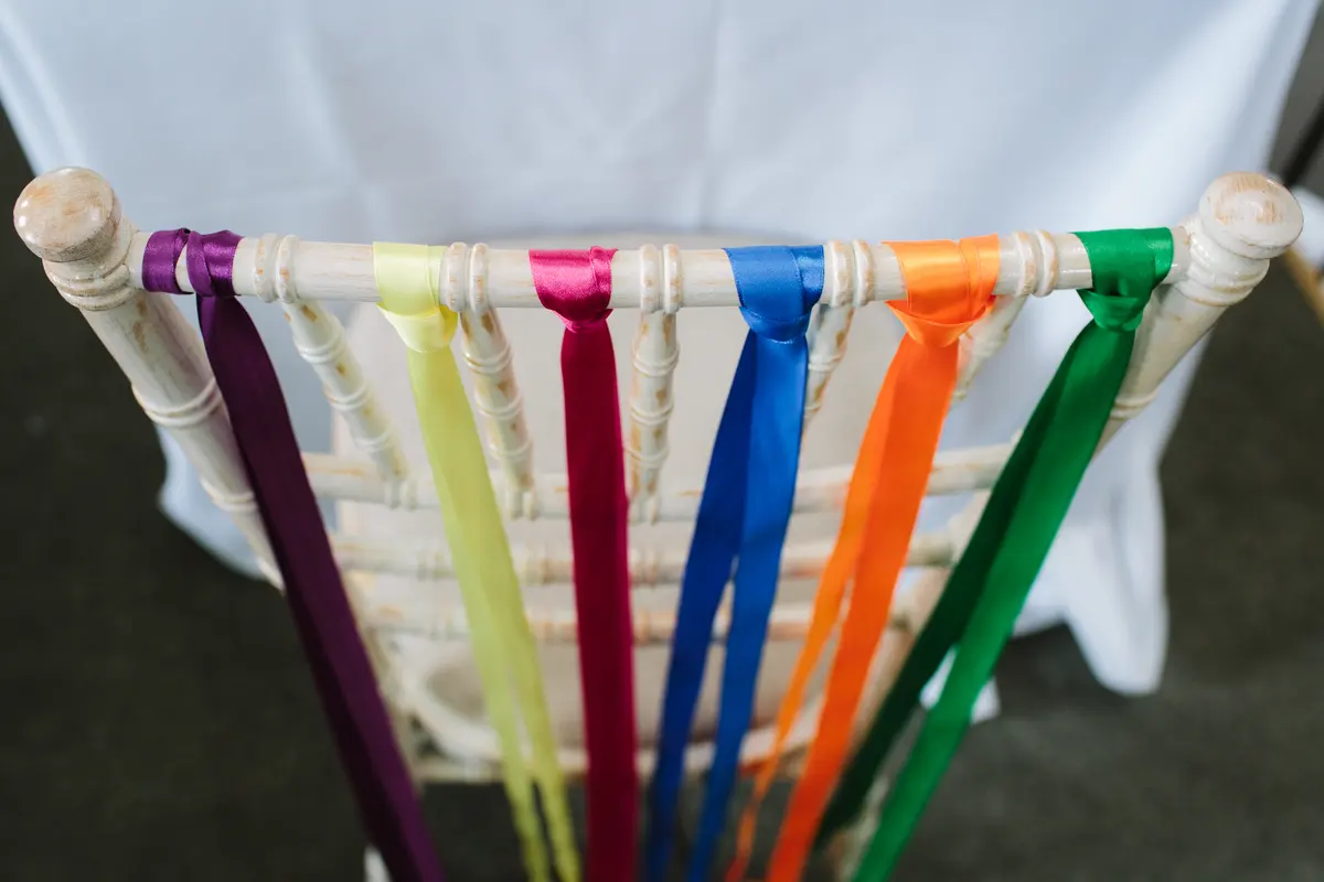 Rainbow of satin ribbons tied to the back of a white chiavari chair