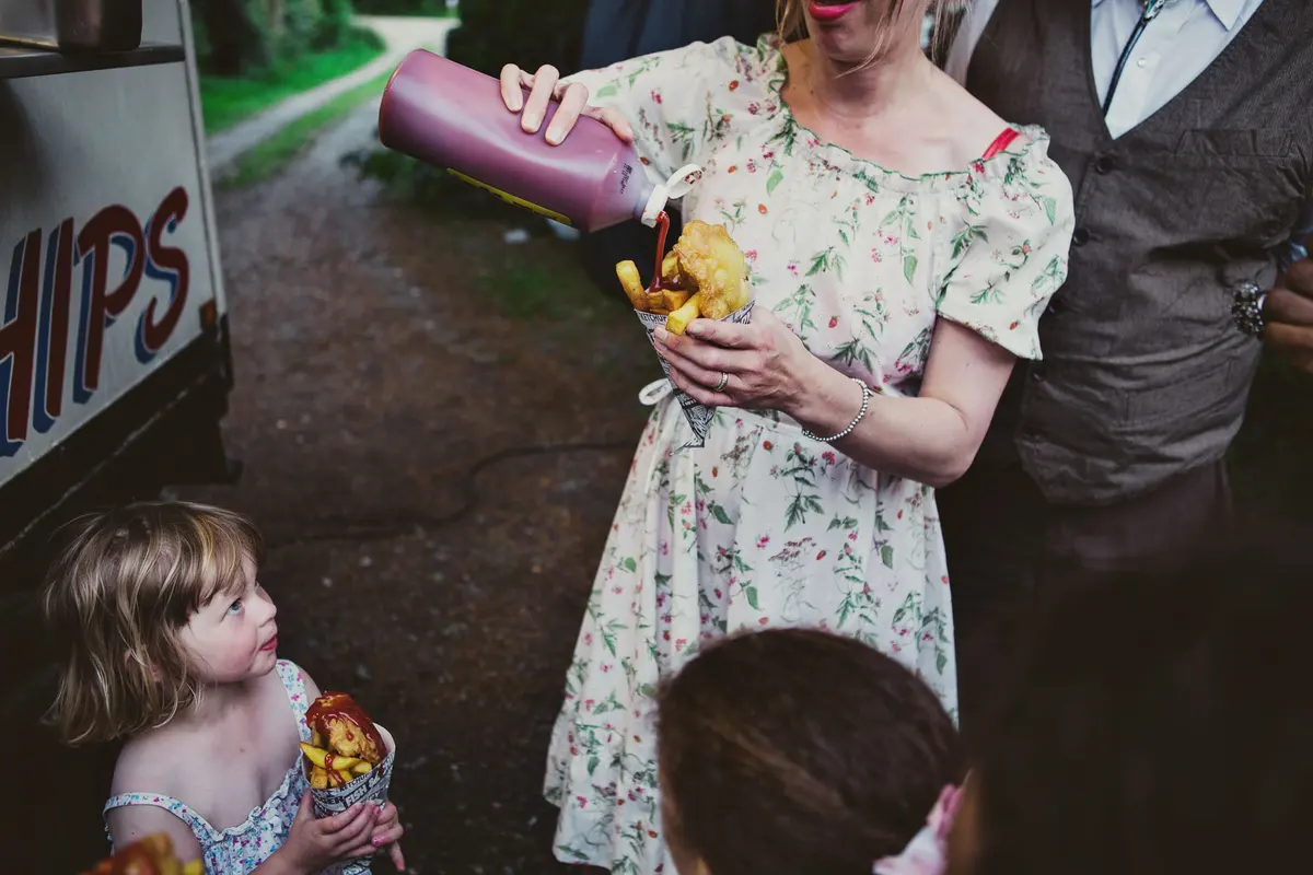 Guest squeezing ketchup on her chips beside a fish and chip van as a little girl looks up