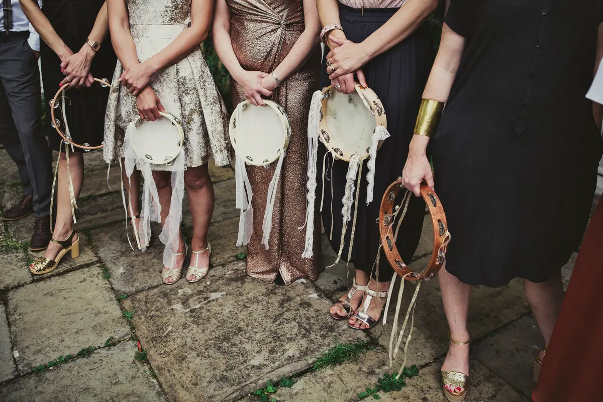 Bridesmaids in metallic dresses and sandals holding tambourines trimmed with ribbons