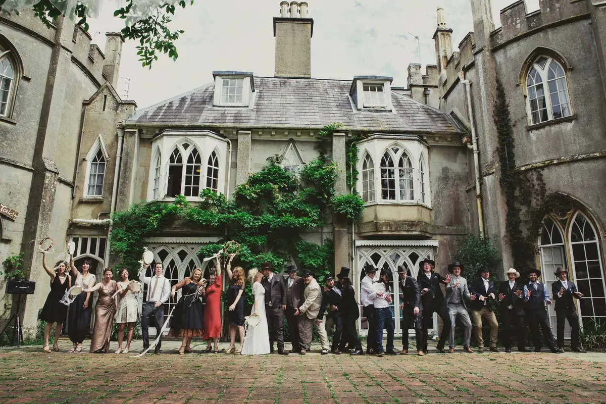 Wedding party cheering in a row in the courtyard of a Gothic house, groomsmen in cowboy hats