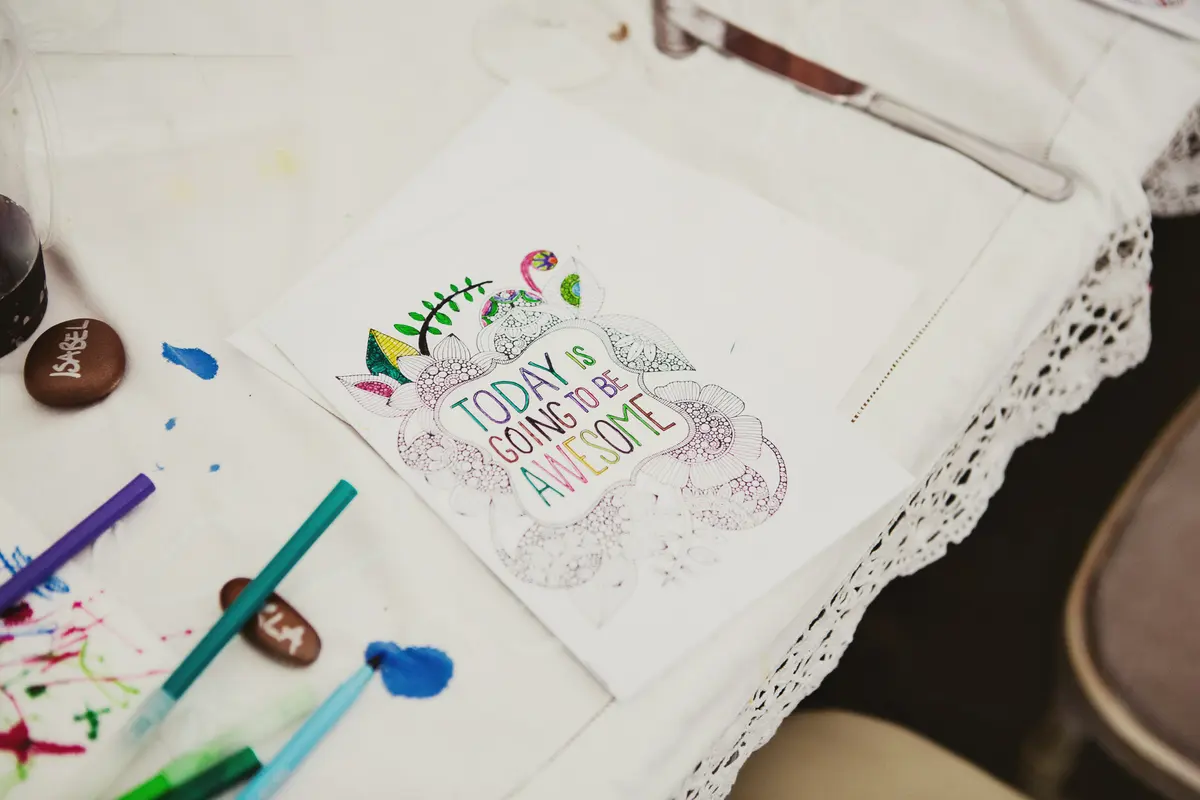 Coloured-in page reading Today is going to be awesome beside felt pens on a lace tablecloth