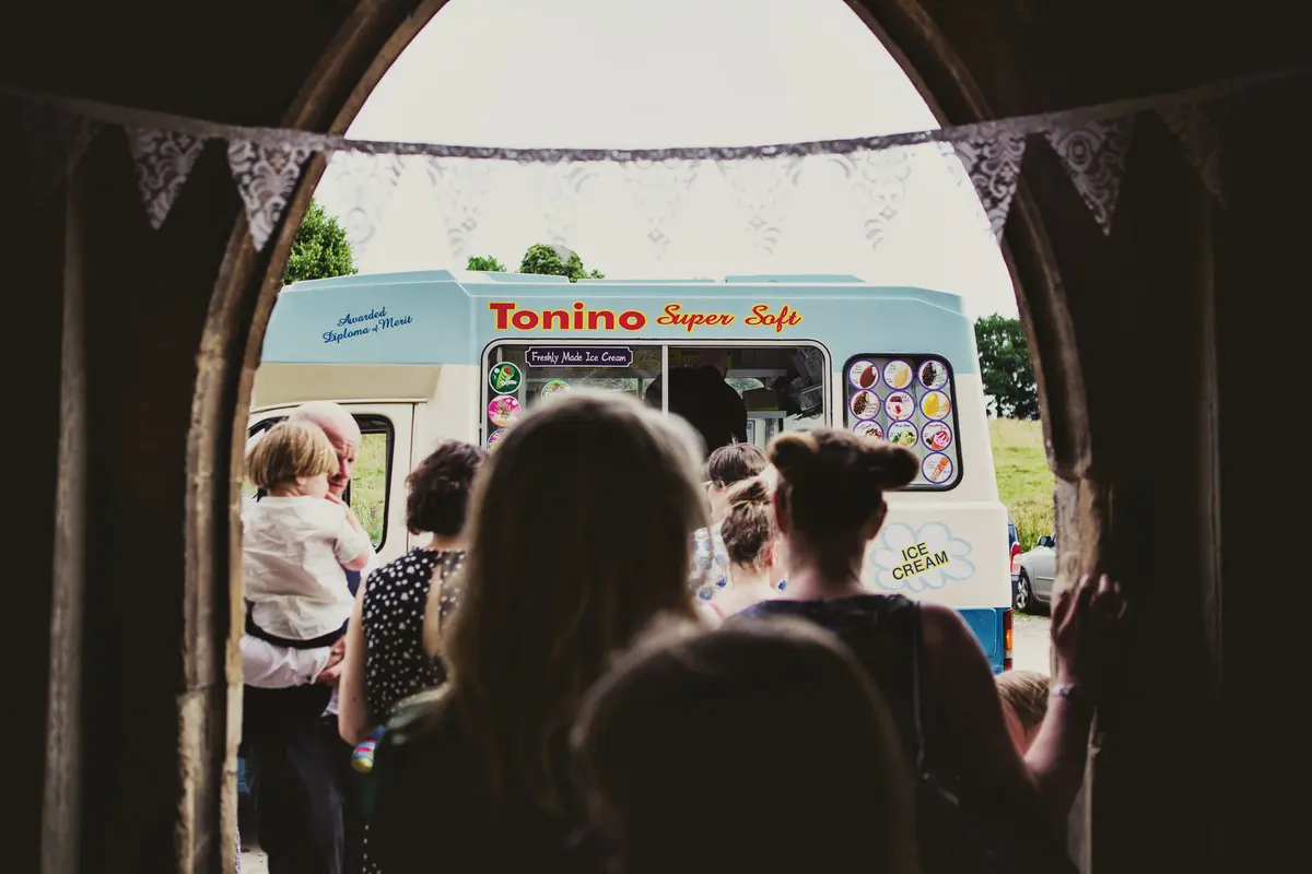 Guests queuing at an ice cream van seen through an arched doorway hung with lace bunting