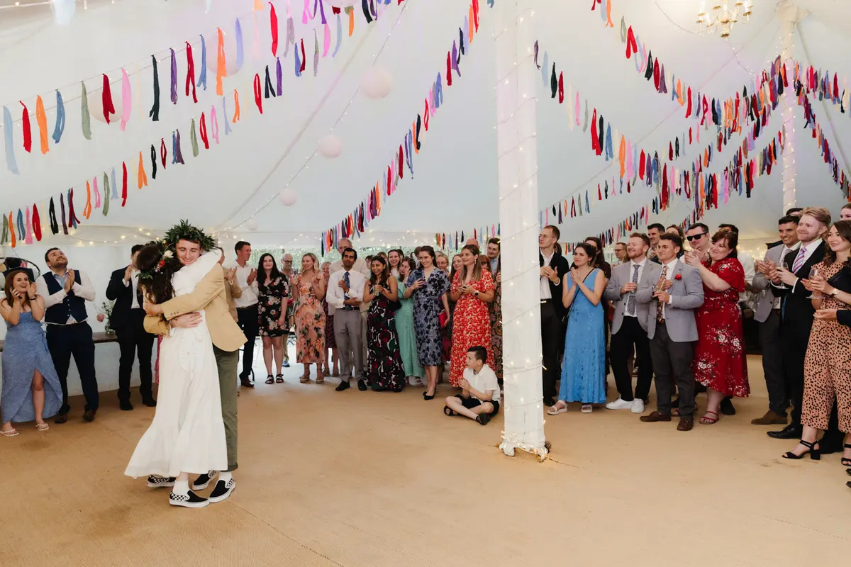 Bride and groom sharing their first dance as guests clap under ribbon bunting in the marquee