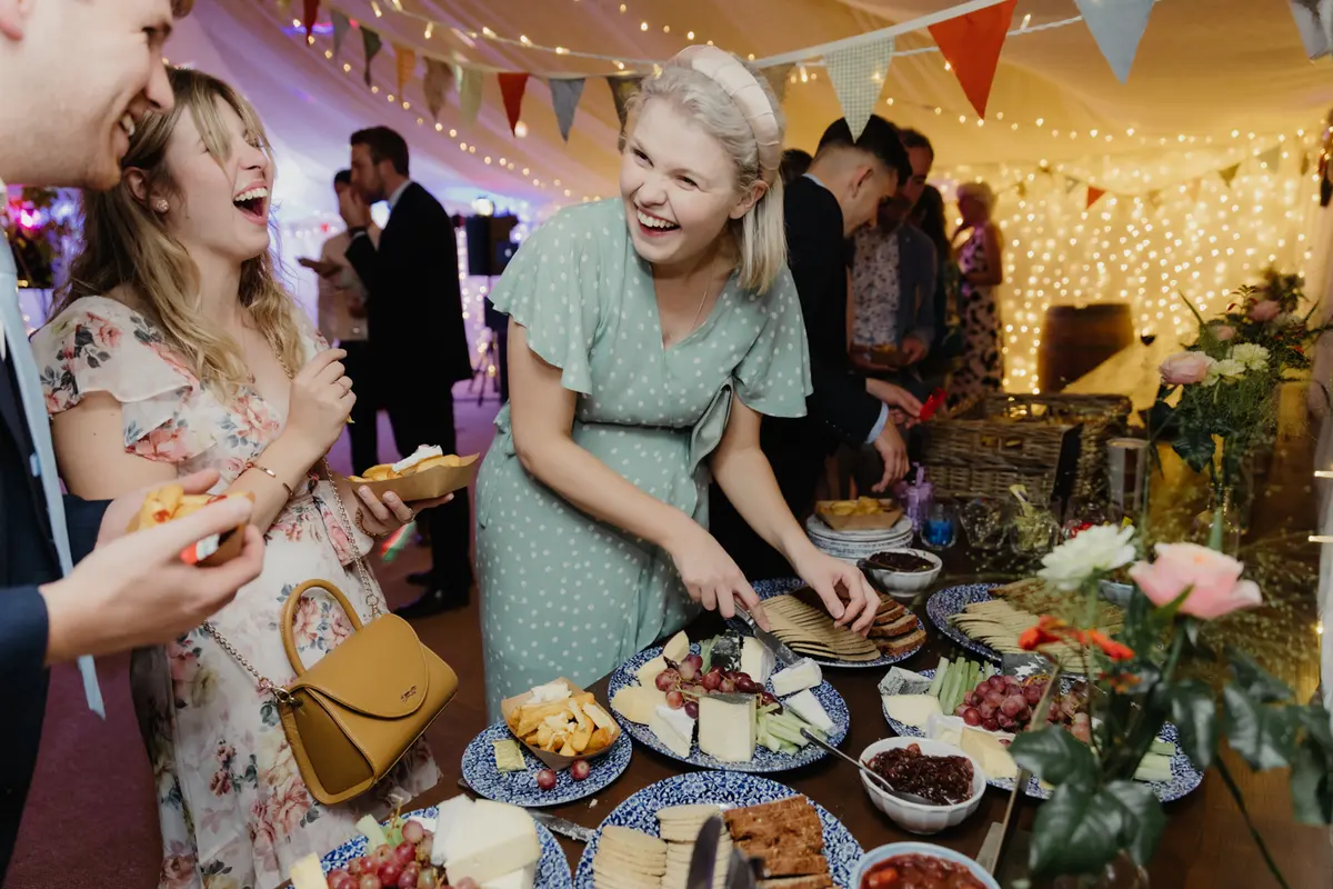Guests laughing as they help themselves from an evening cheese board in the marquee