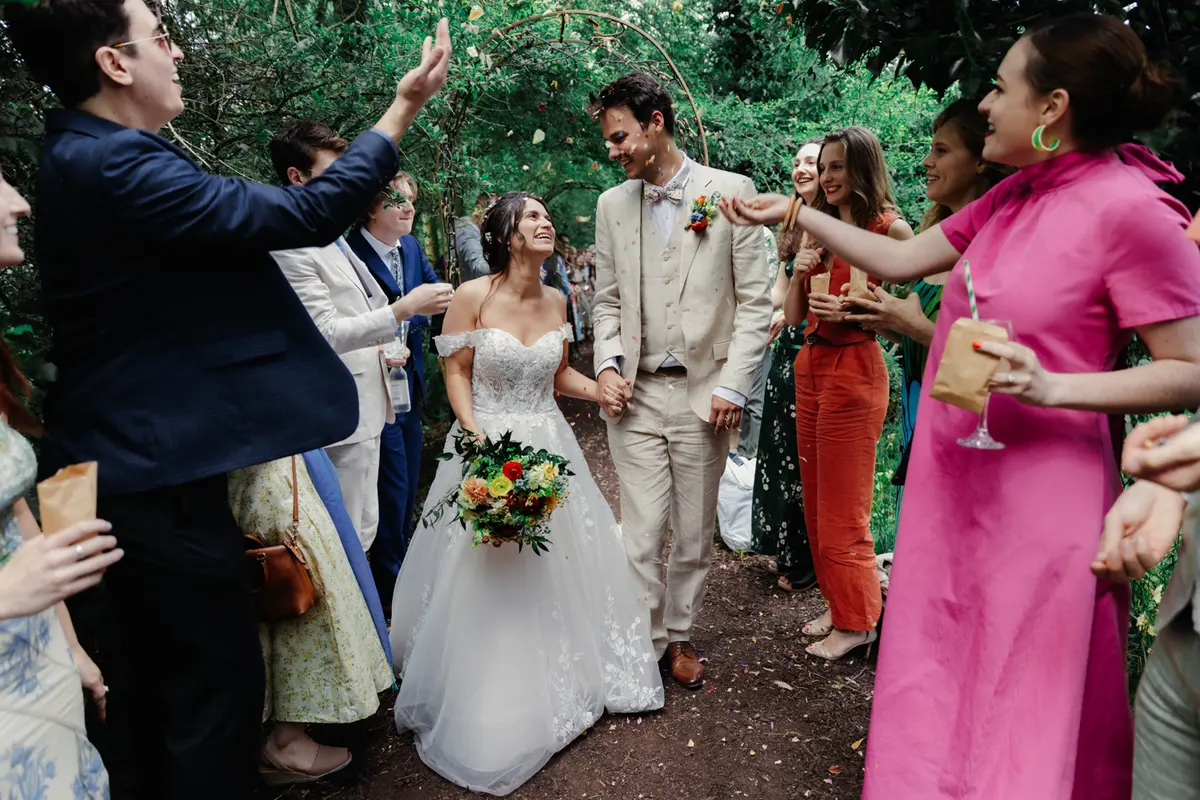 Bride and groom walking through a line of guests throwing confetti on a garden path