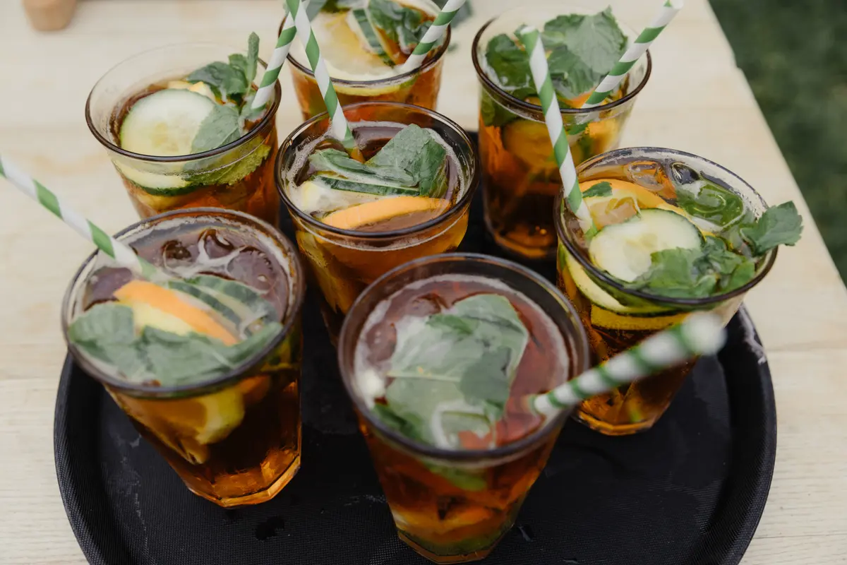 Tray of Pimm's with cucumber, orange and mint in glasses with striped straws