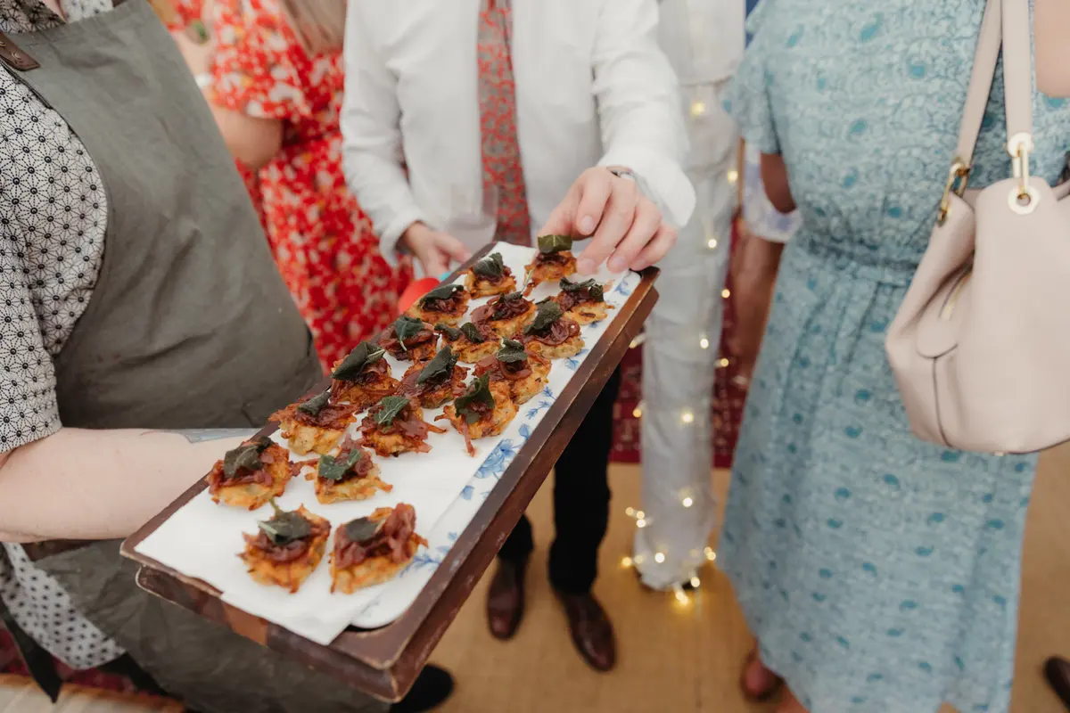 Guest taking a canapé from a wooden tray carried by a waiter in an apron