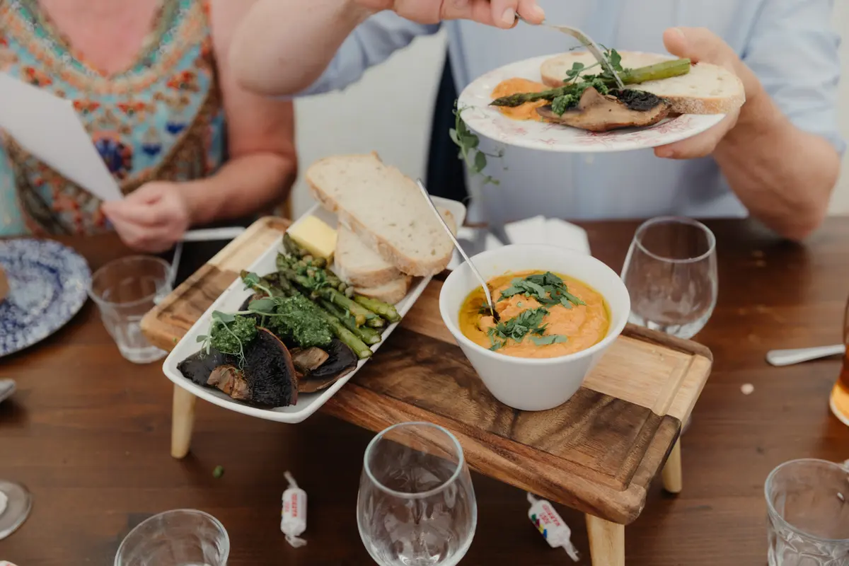 Guests serving themselves from sharing boards of soup, bread and roasted vegetables