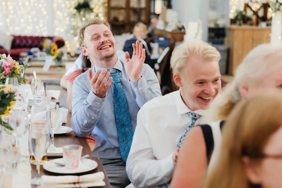 Two guests laughing and clapping during the speeches in the marquee