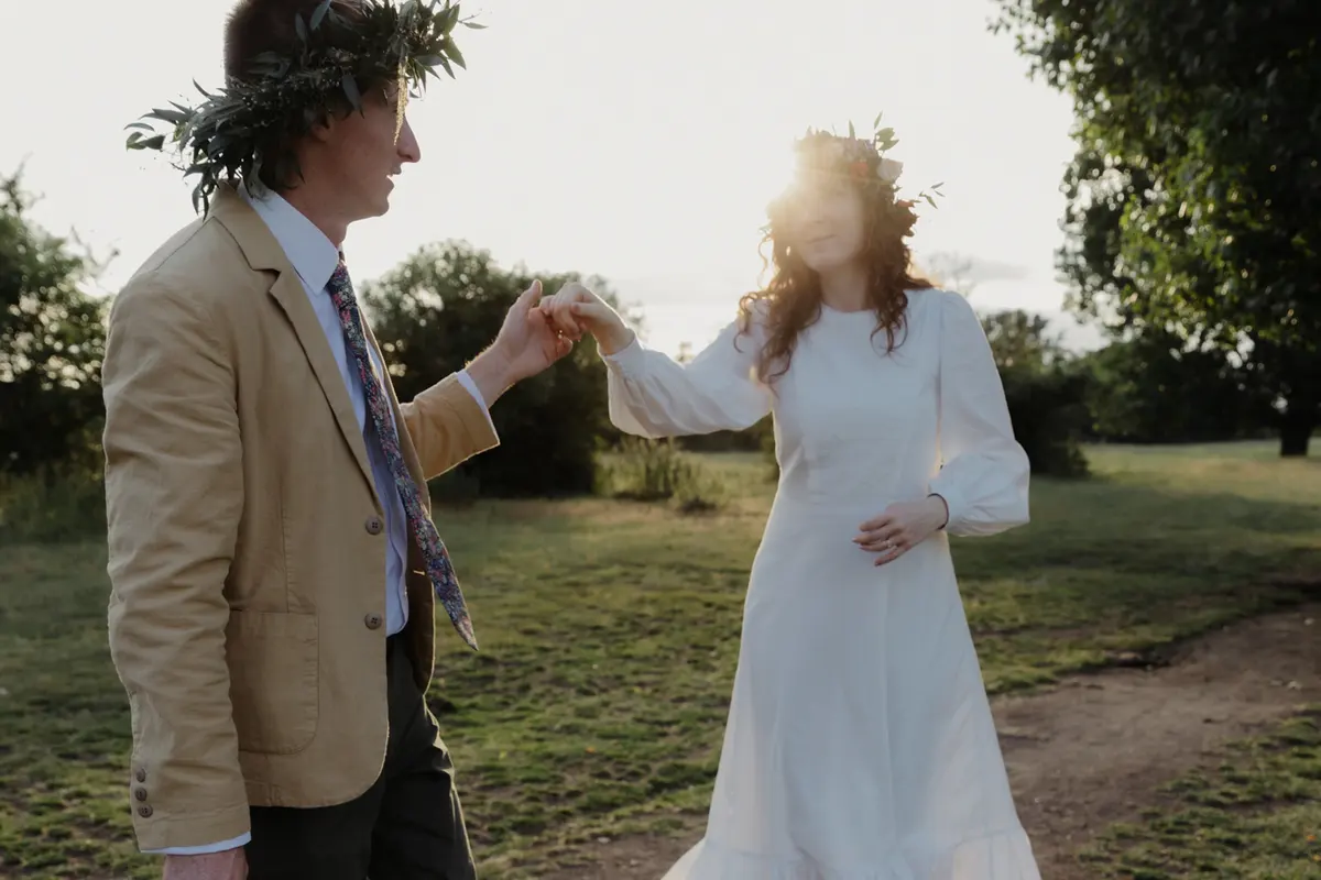 Groom in a leaf crown twirling the bride by the hand in evening sunlight