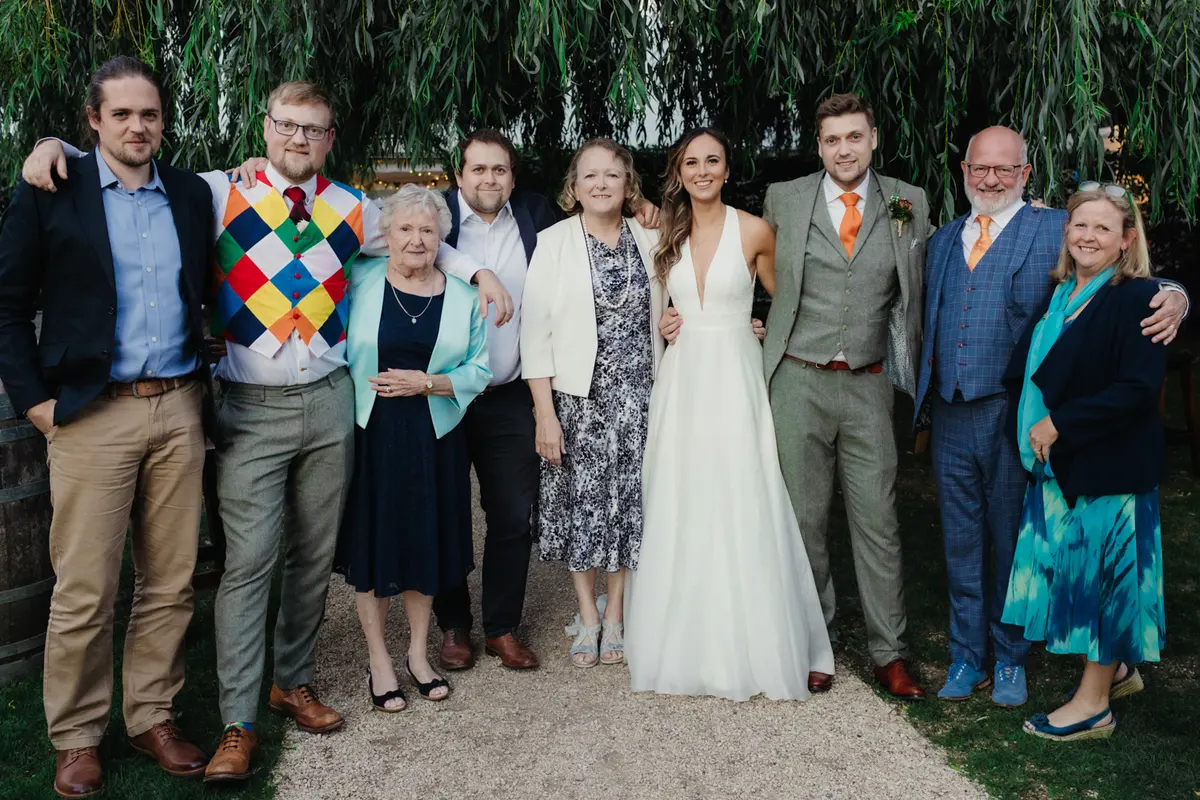 Bride and groom standing with family in front of a willow tree