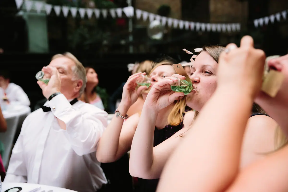 Wedding guests downing green shots together under white bunting
