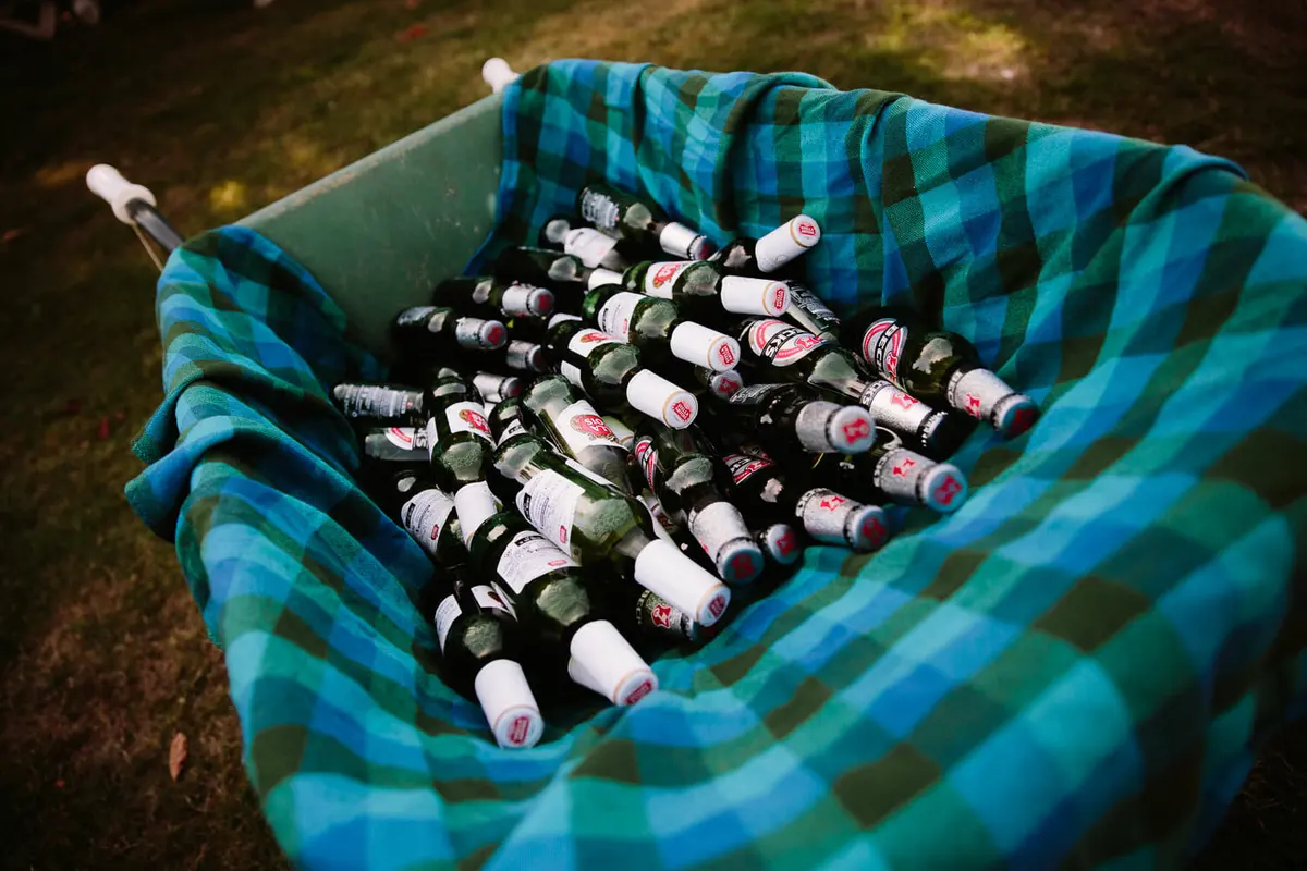 Wheelbarrow lined with a checked blanket and filled with bottles of beer on the grass
