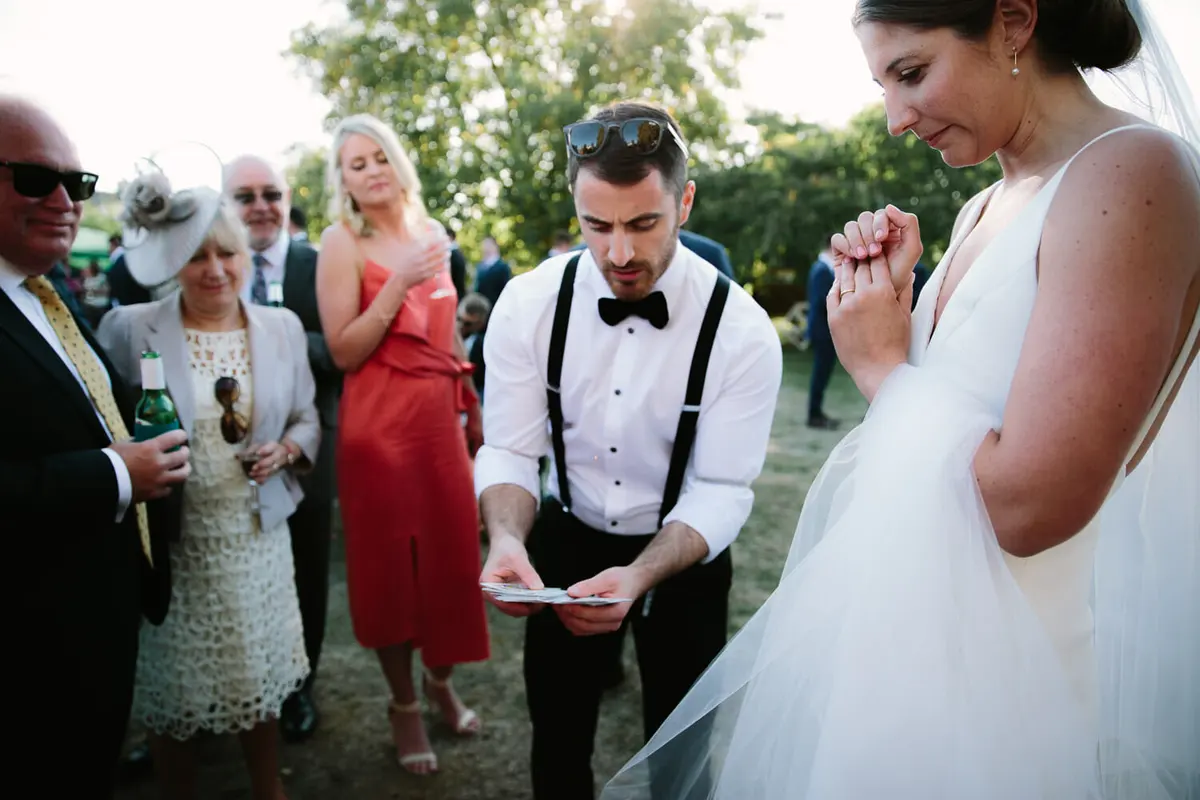 Magician in braces and bow tie performing a card trick for the bride and guests on the lawn