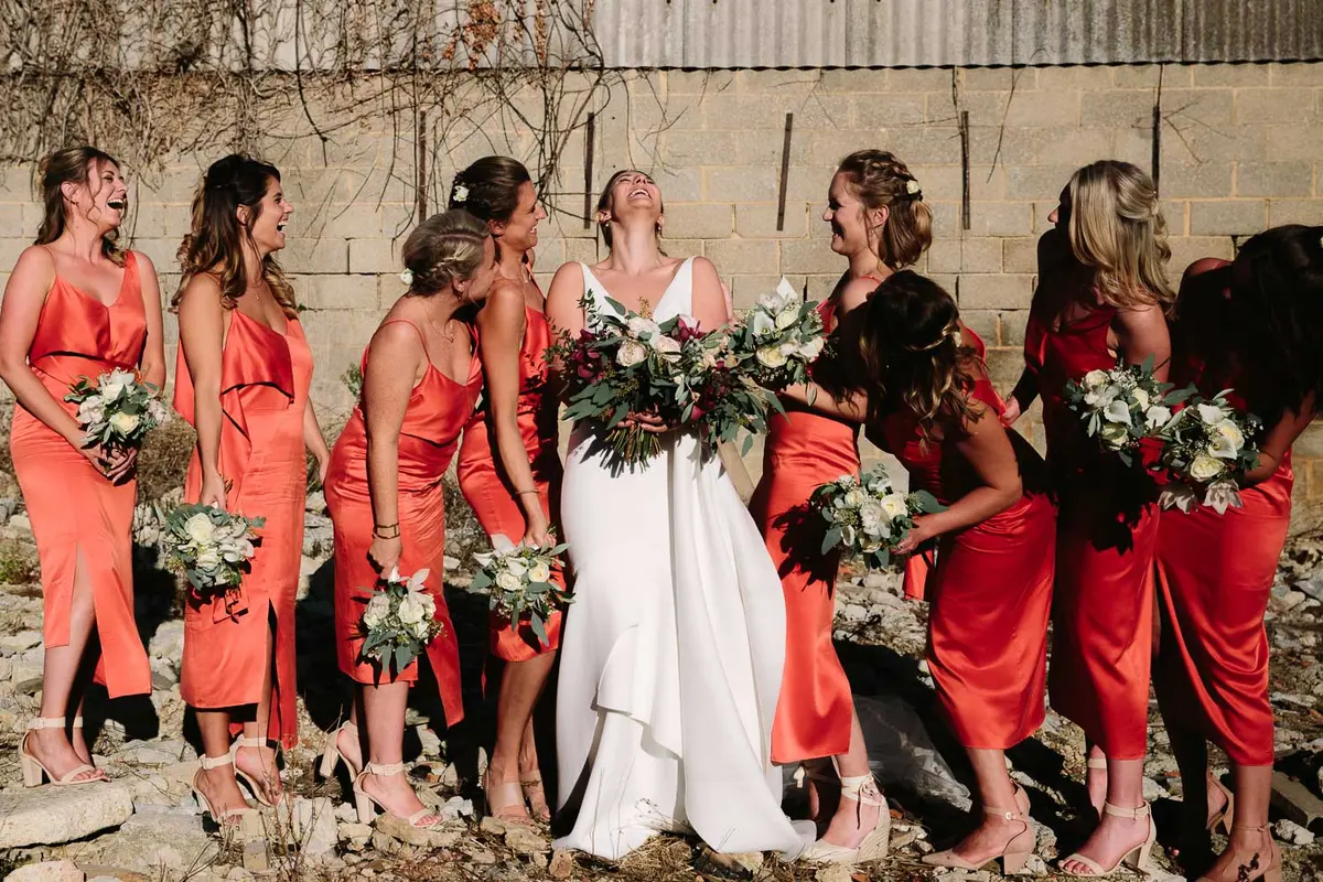 Bride in white laughing with bridesmaids all in orange dresses, at Manor Farm Barn Wedding venue