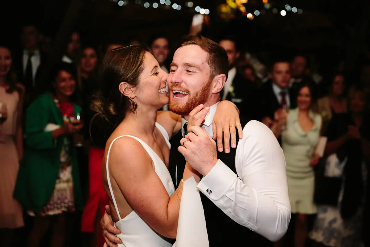 Bride and groom laughing and embracing on a crowded dance floor at night
