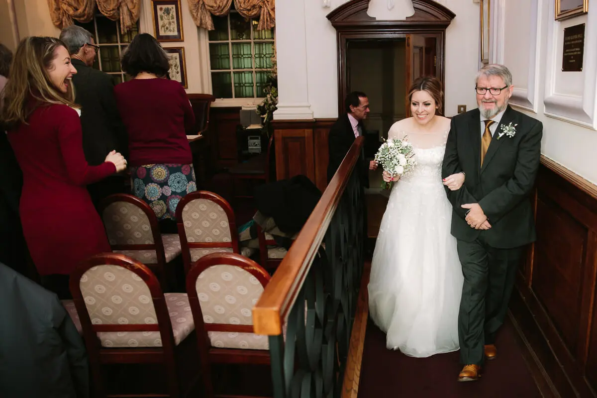 Bride walking down the aisle on her father's arm as smiling guests turn to watch