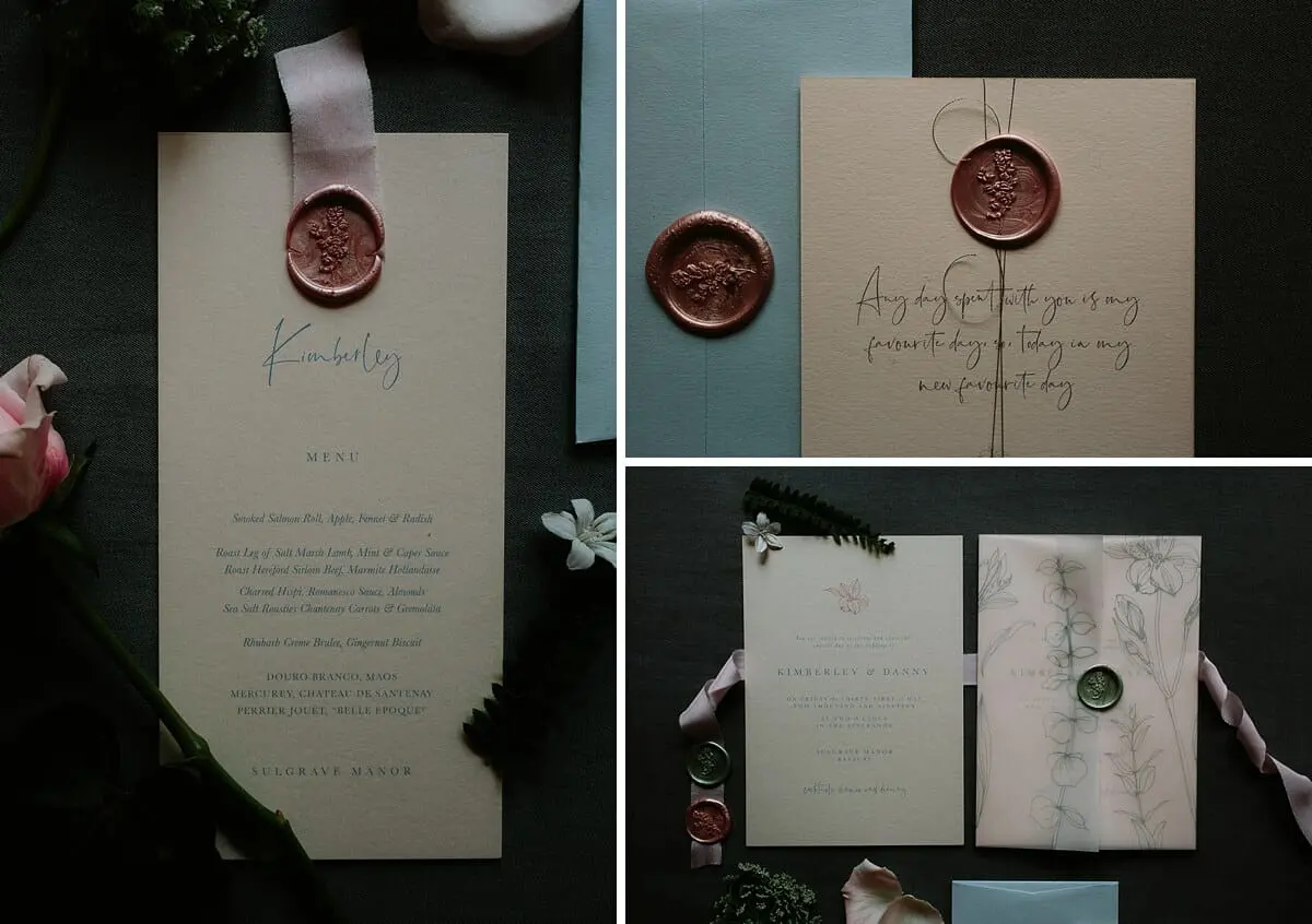 Wedding menu and invitations with pink wax seals, ribbon and pressed flowers laid on dark slate
