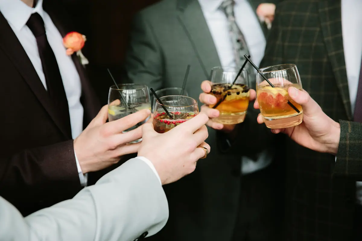 Groomsmen clinking tumblers of cocktails with fruit and black straws