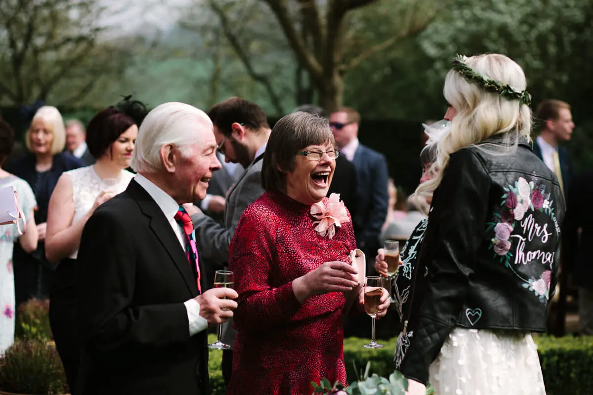 Older guests laughing with glasses of fizz as they chat with the bride in her painted leather jacket