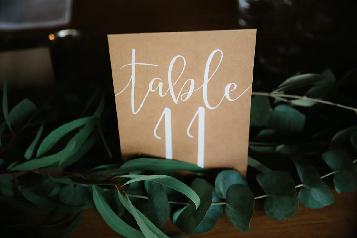 Kraft paper table number 11 card with white calligraphy on a bed of eucalyptus