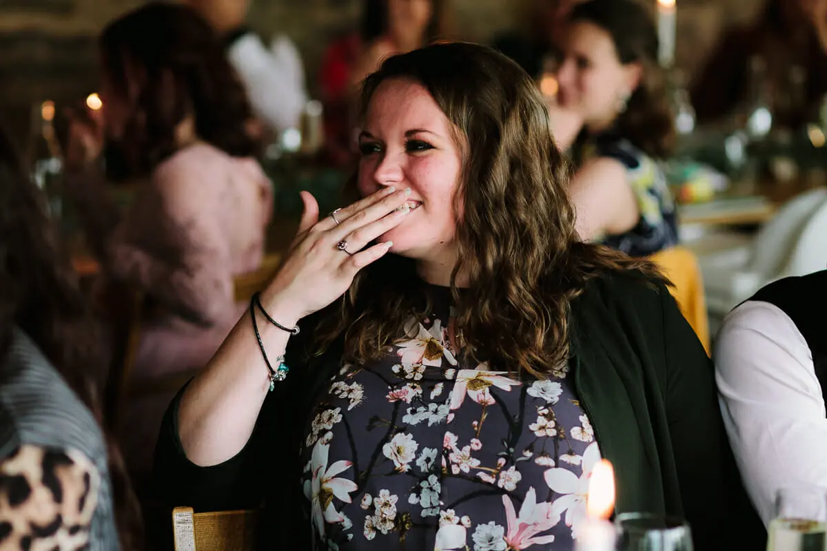 Wedding guest in a floral dress blowing a kiss from a candlelit reception table
