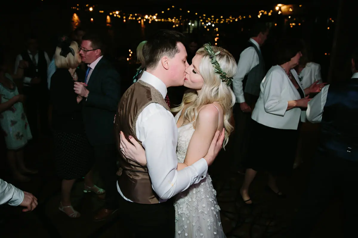 Bride and groom kissing on a crowded dance floor at night