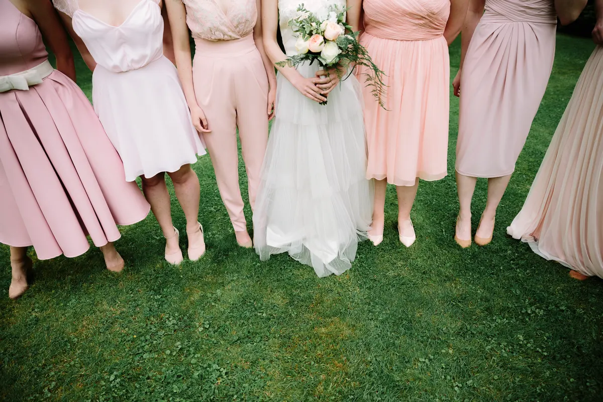 Bride and bridesmaids in mismatched pink dresses standing in a row on the lawn