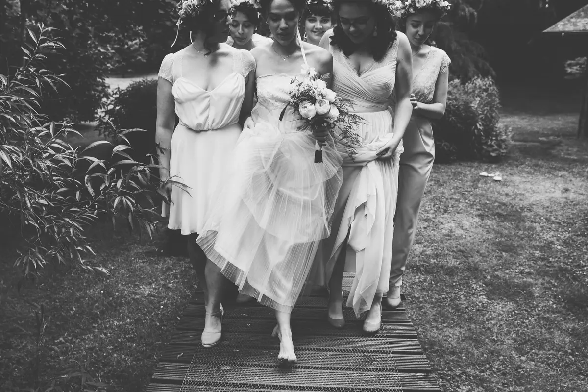 Black and white shot of the bride walking arm in arm with her bridesmaids along a boardwalk
