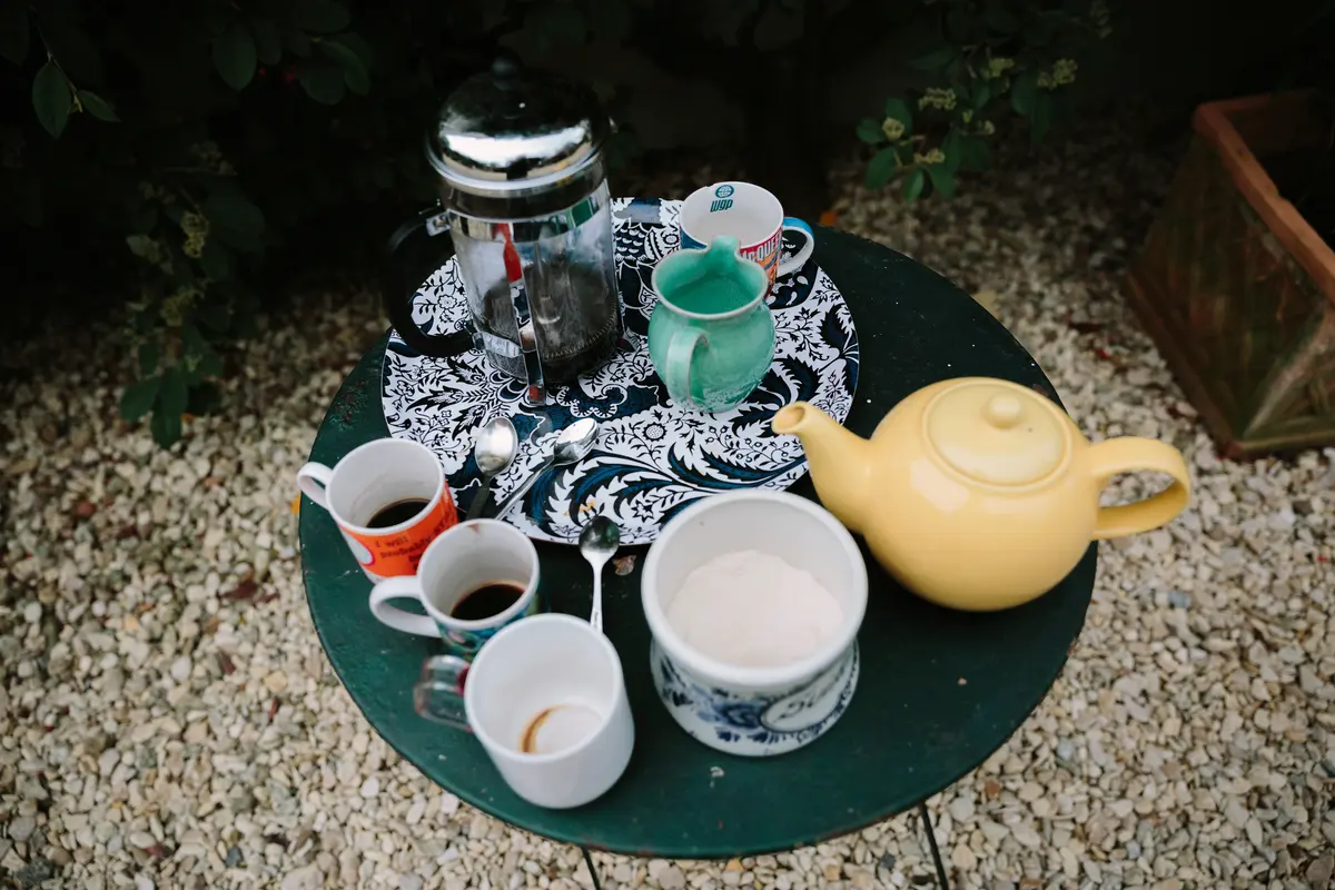 Cafetière, yellow teapot and mugs on a small green garden table on gravel