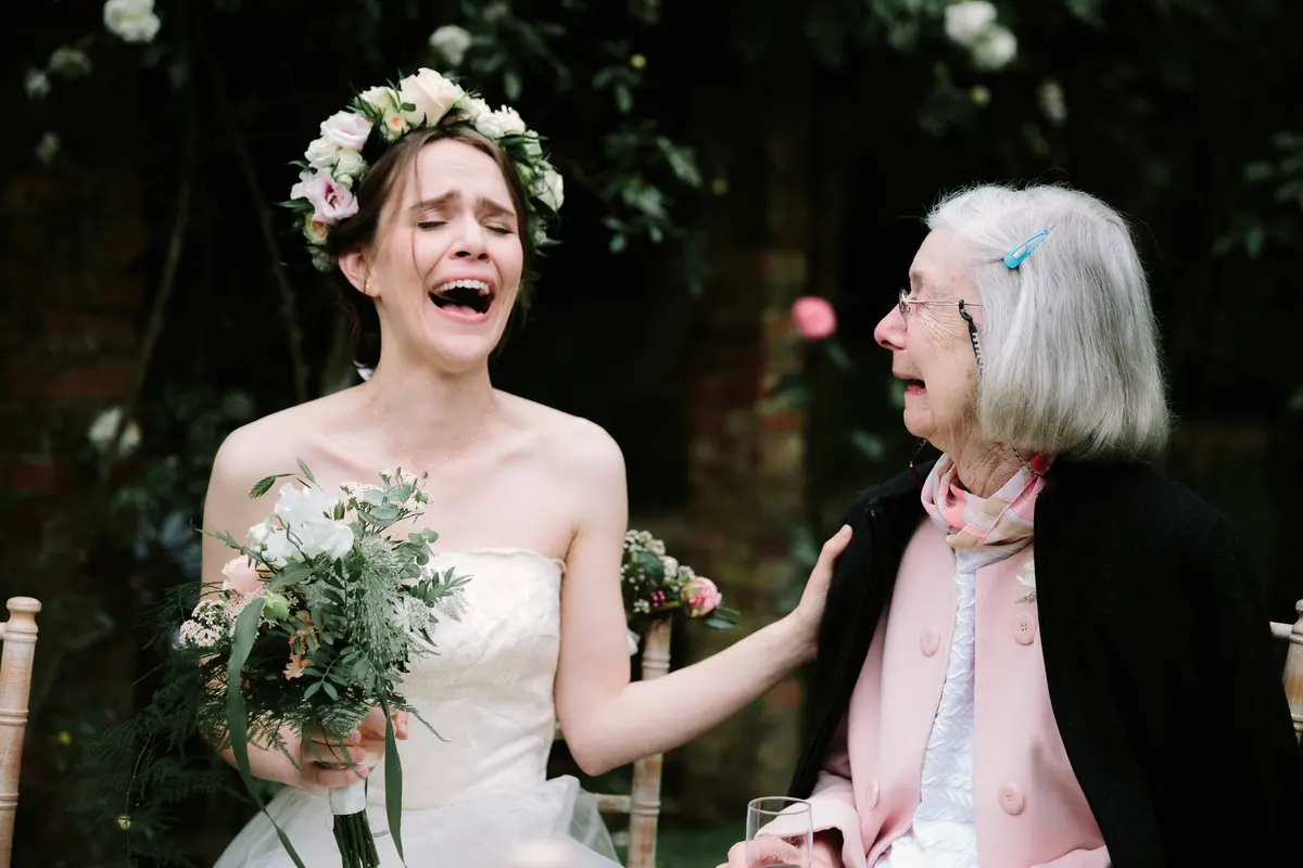 Bride in a flower crown laughing with an older woman in a pink jacket