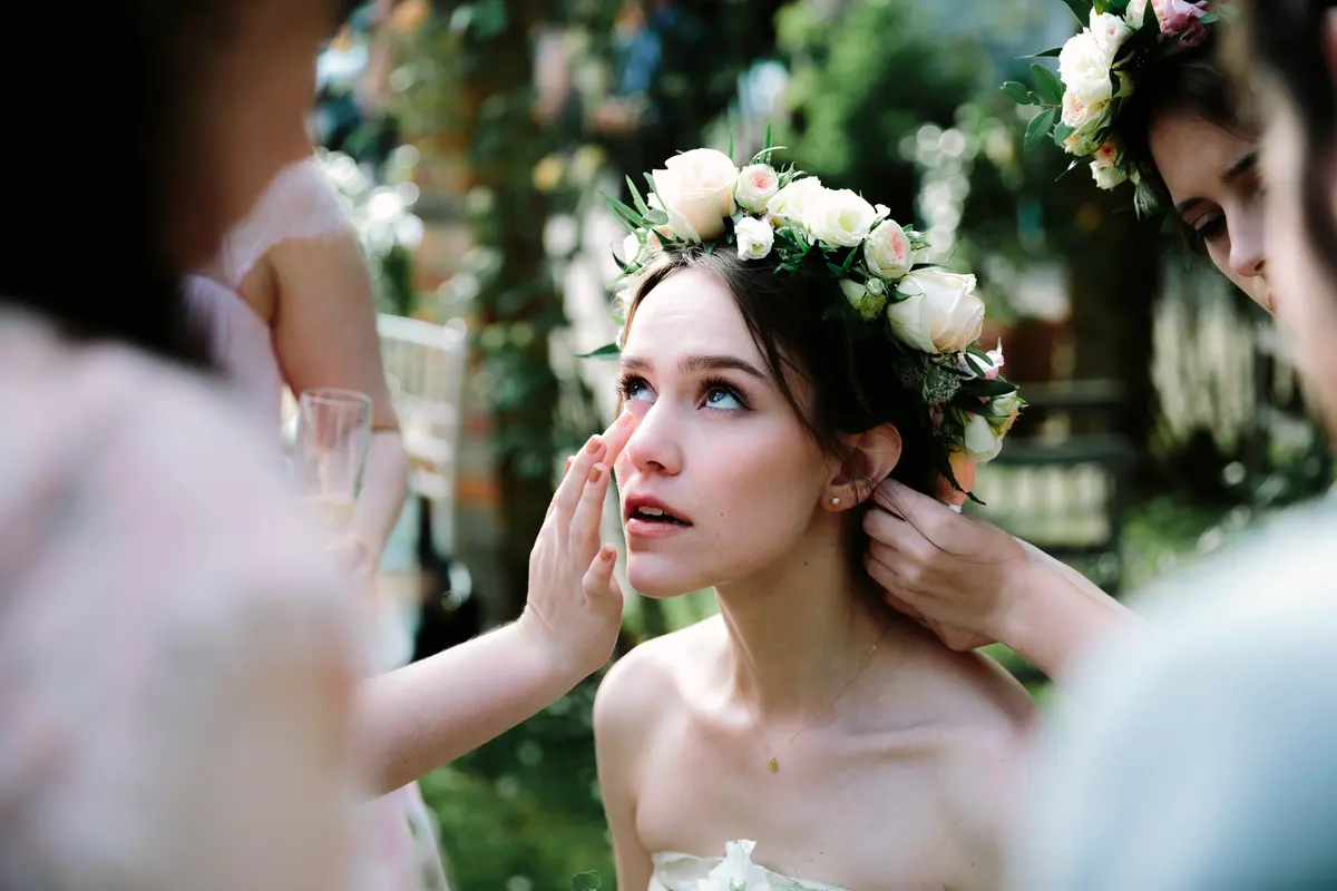 Bride wiping a tear while a bridesmaid adjusts her rose flower crown
