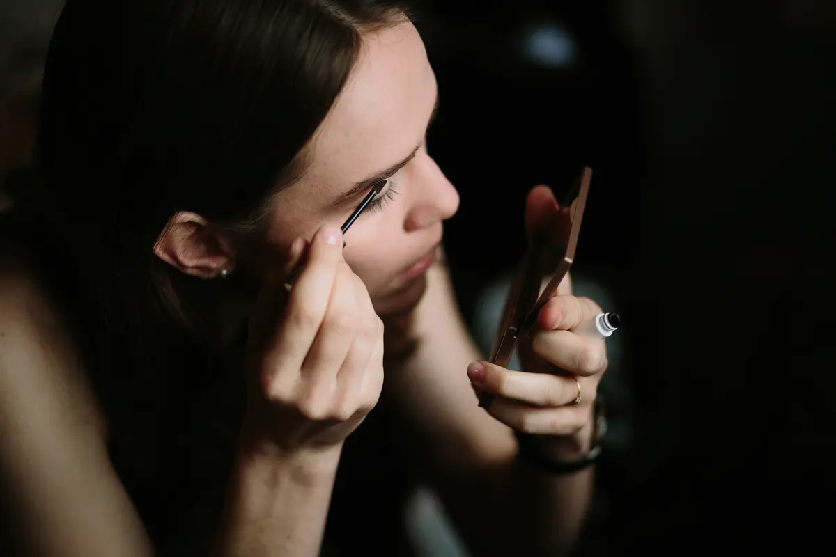 Woman applying mascara while holding a small compact mirror