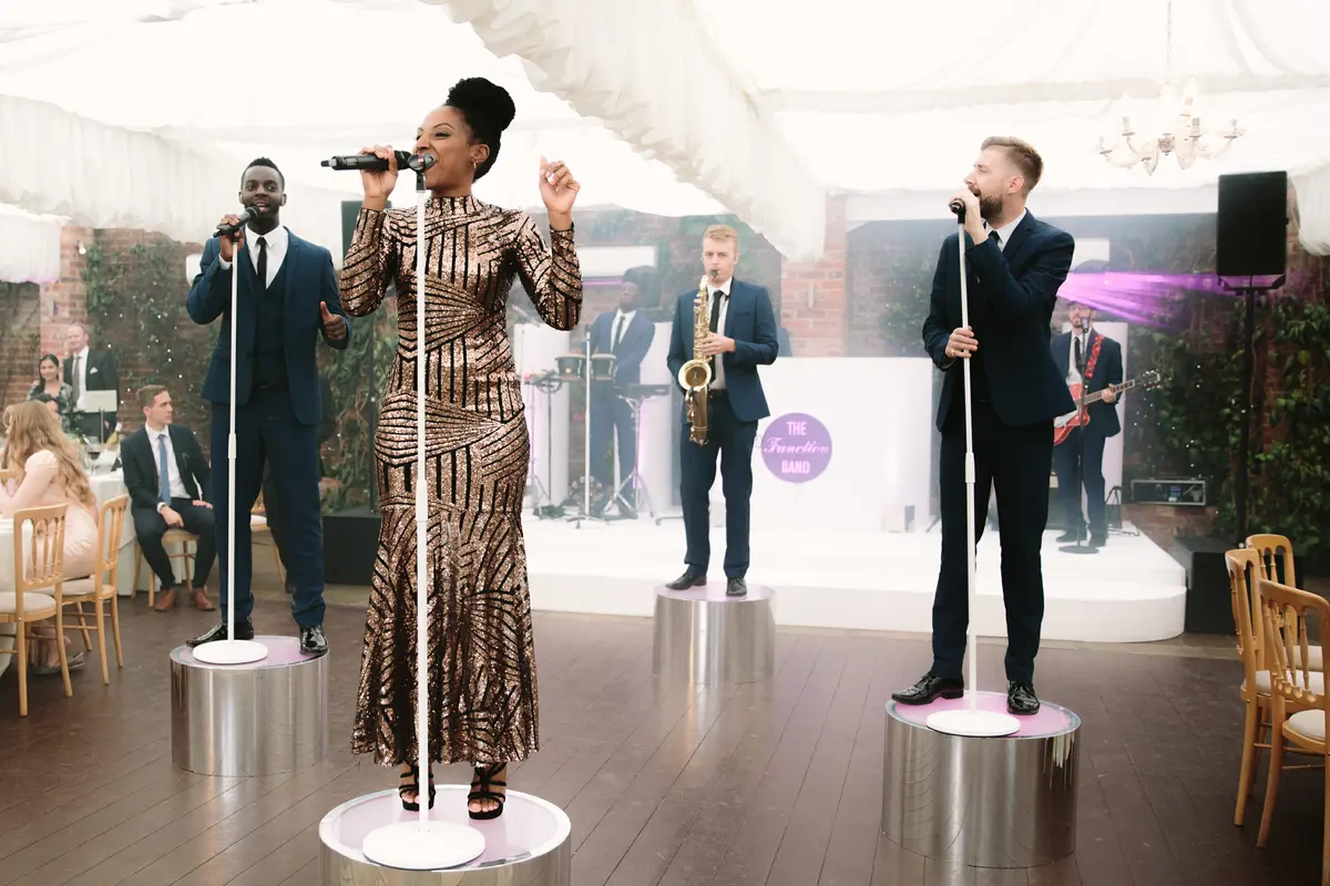 Live band singers performing on mirrored podiums in a marquee with a saxophonist behind