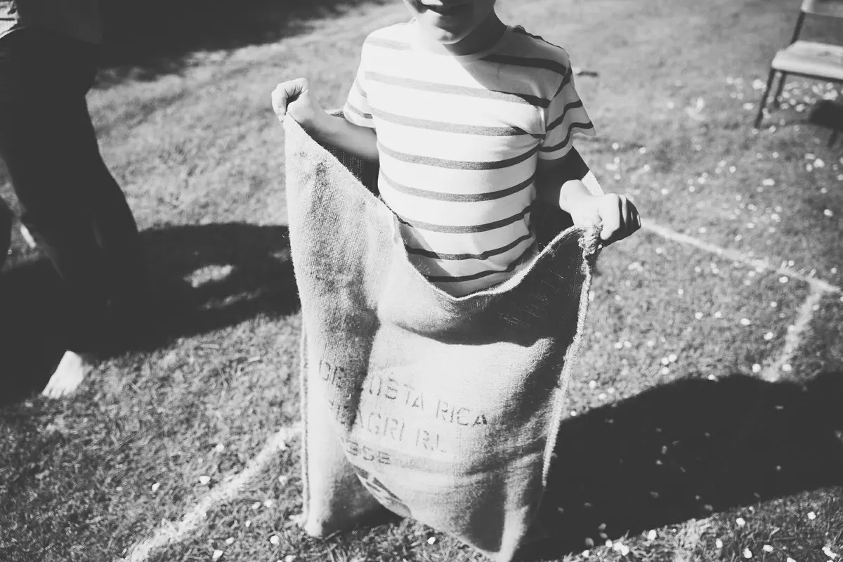 Black and white shot of a child in a striped top standing in a sack for a sack race