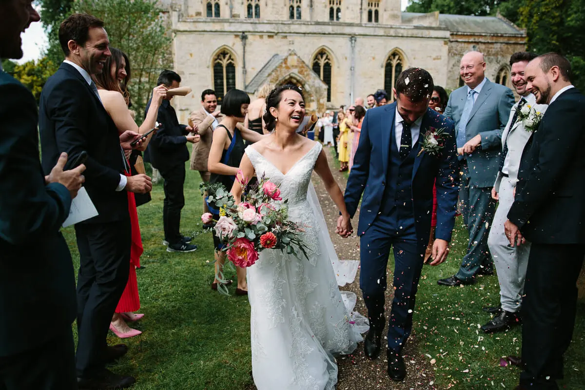 Bride with a pink and coral bouquet and the groom walking through a confetti line of guests