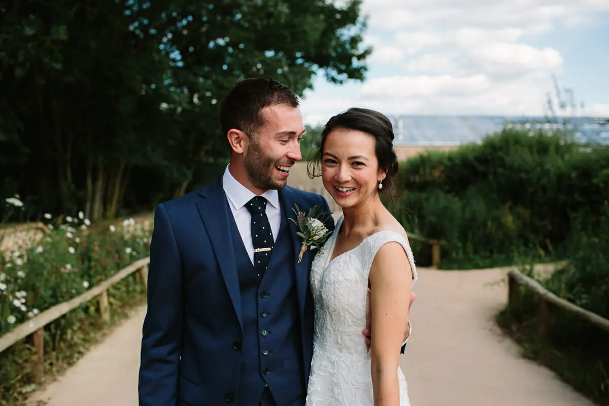 Bride and groom smiling together on a path lined with wild flowers at Soho Farmhouse