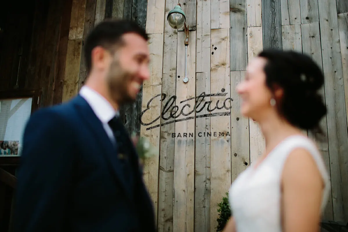 Bride and groom smiling at each other, out of focus, in front of the Electric barn cinema sign