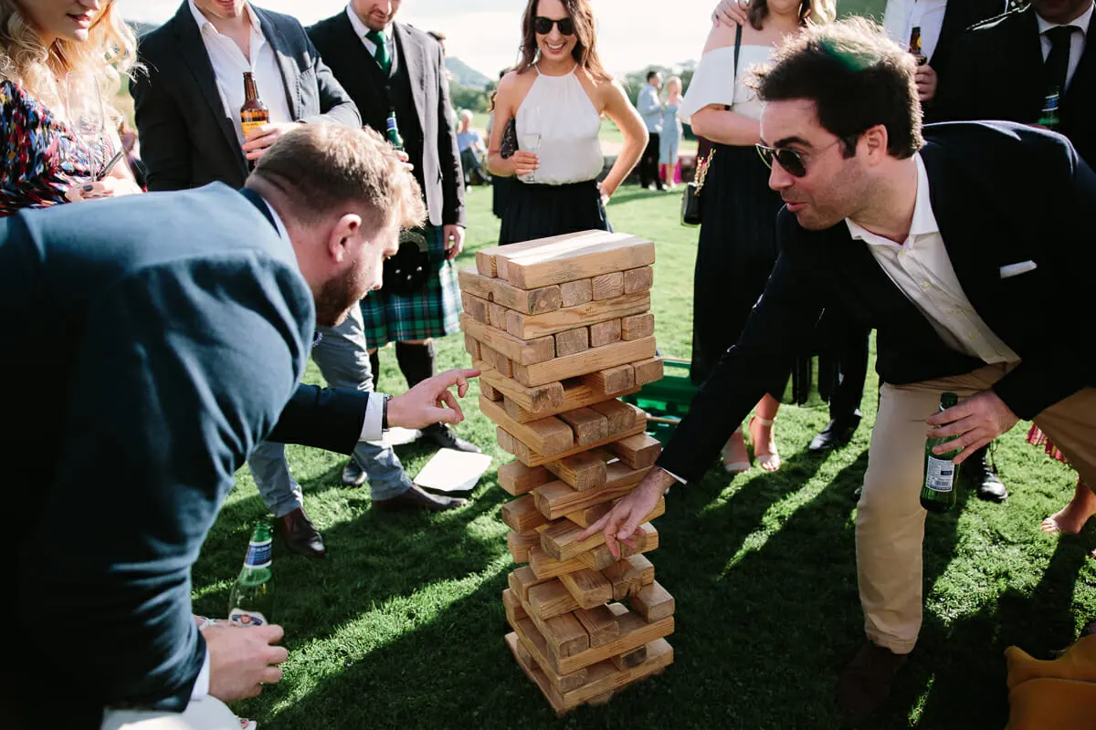 Wedding guests crowding round a giant Jenga tower on the lawn in the sunshine