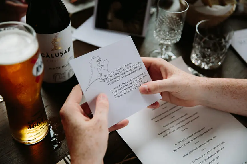 Guest reading a card inviting them to draw a dinosaur, beside a menu, beer and wine