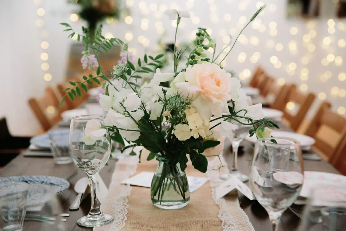 Peach rose and sweet pea posy in a jar on a hessian runner, with fairy lights behind, at the Perch