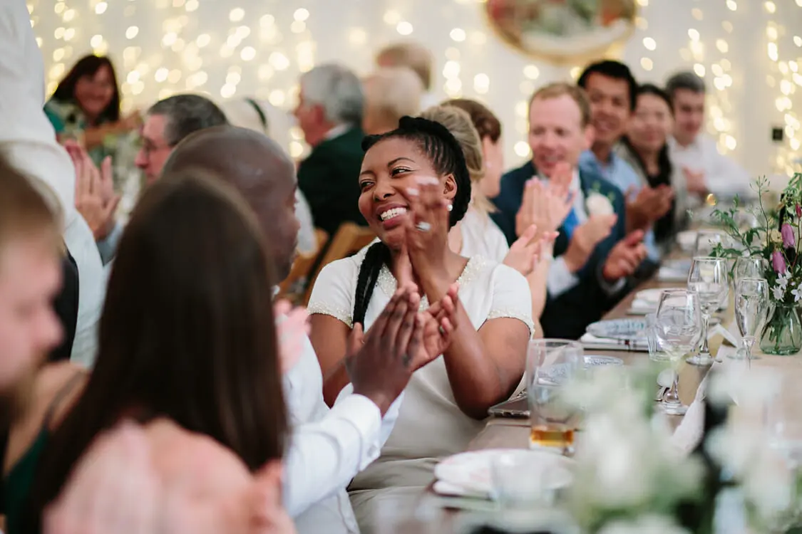 Guest laughing and clapping during the speeches in a marquee lit with fairy lights at the Perch