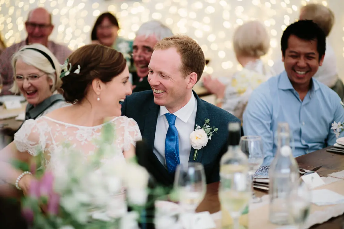 Bride and groom laughing together at the top table with guests behind them