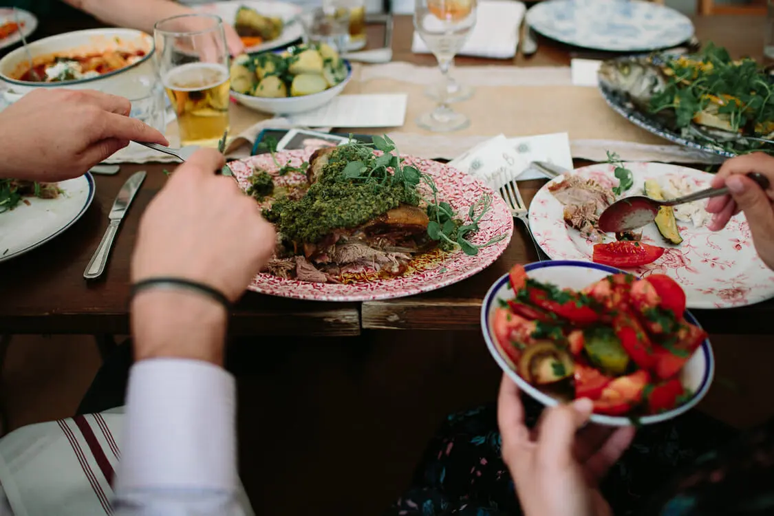 Guests sharing a lamb dish with green herb sauce and a tomato salad at a wedding breakfast