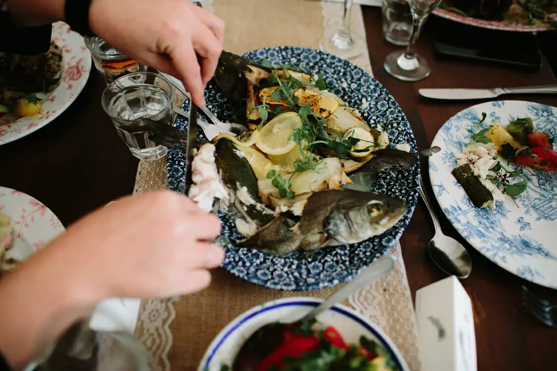 Guest serving whole baked fish with lemon from a blue and white platter on a lace runner
