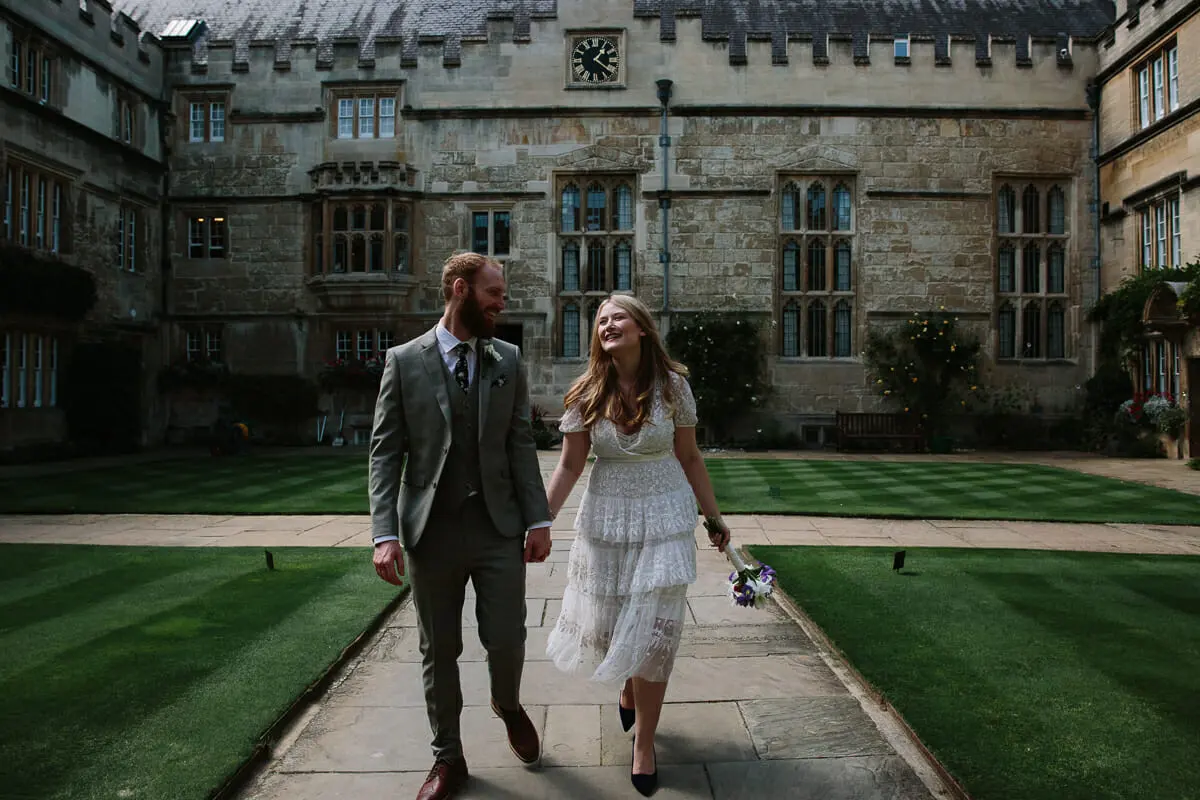 Bride and groom walking hand in hand along the path of an Oxford college quad
