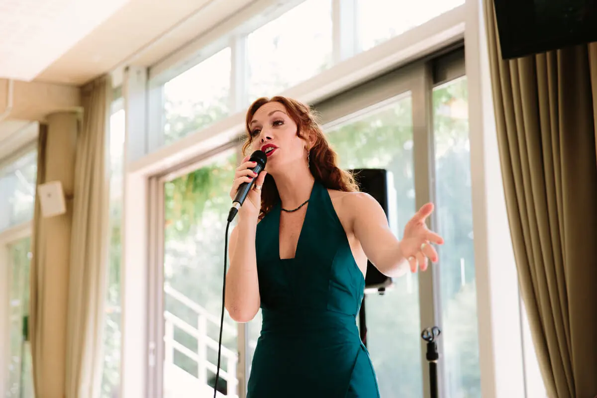 Singer in a green halterneck dress performing with a microphone by tall windows