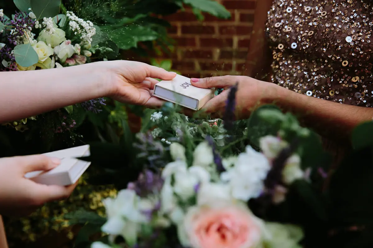 Bridesmaid being handed a small gift box beside a bouquet of white and pink flowers